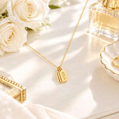 Collier tag prénom gravé or en scène lifestyle – coiffeuse blanche, roses, Kylara